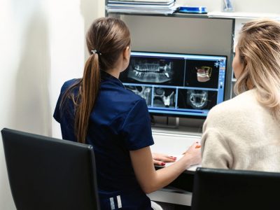 Female doctor shows the patient an x-ray image at display. Computer diagnostics dental tomography. Planning teeth treatment in modern dental clinic